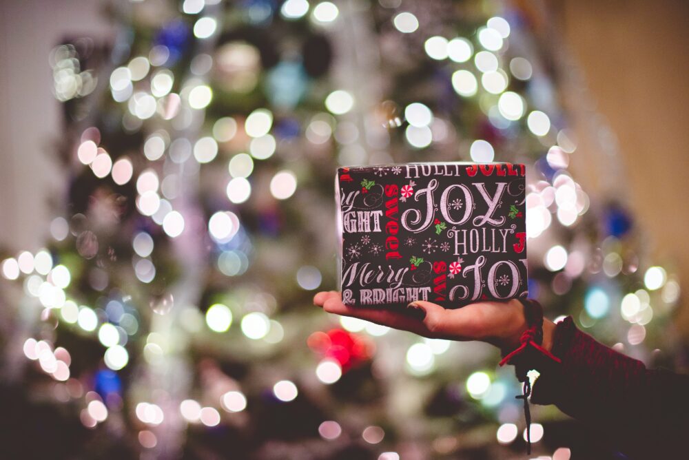 An in-focus Christmas present held up infront of a blurred out Christmas tree