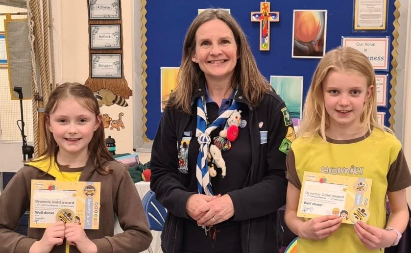A Girlguiding leader stands in between two Brownies holding certificates